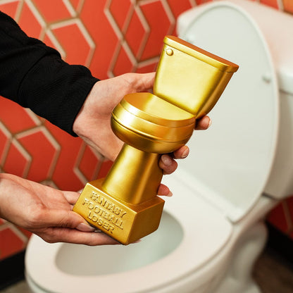 Hands holding a gold trophy shaped like a toilet with "Fantasy Football Loser" engraved, in front of a white toilet.