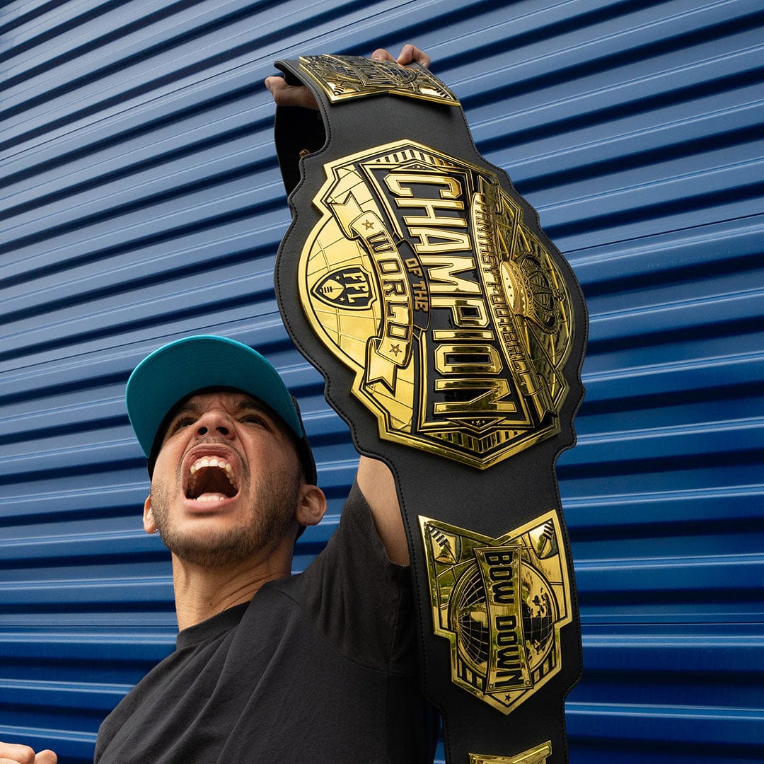 Man wearing a teal cap holding up a large gold and black "Champion of the World" championship belt.