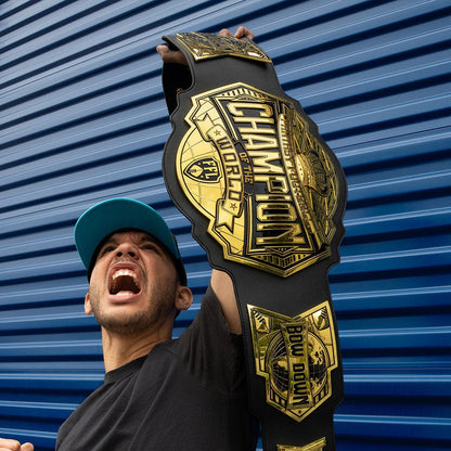 Man wearing a teal cap holding up a large gold and black "Champion of the World" championship belt.